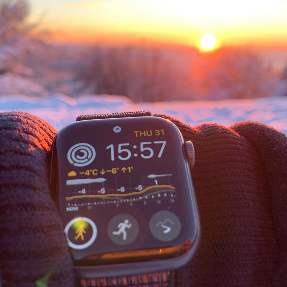 Apple Watch on wrist showing Weathergraph weather complication with temperature curve and snow forecast in snowy winter landscape